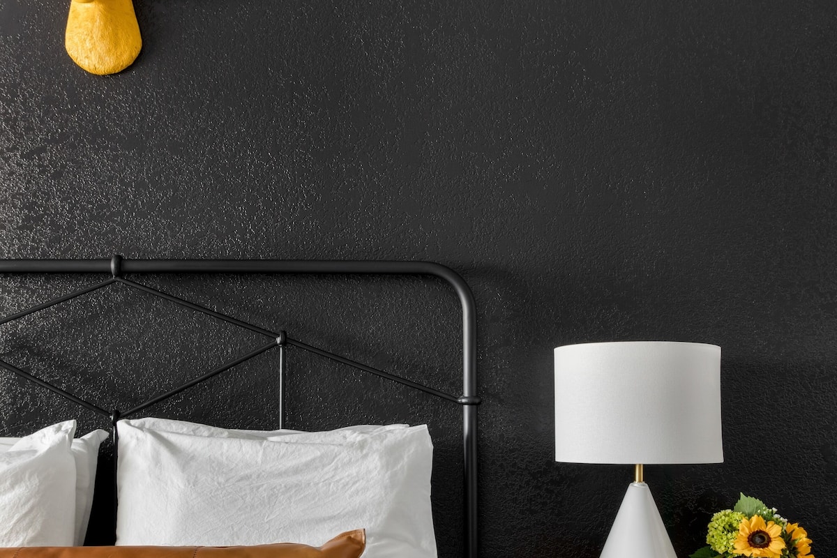 Uma cama com roupa de cama branca e marrom, um criado-mudo de madeira com uma luminária e uma cabeça de veado fixada na parede.