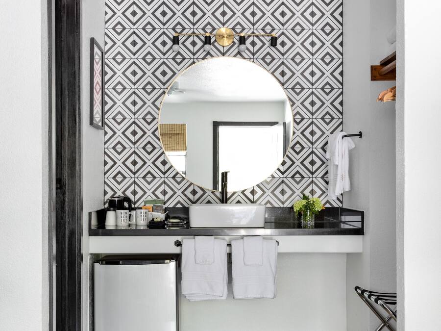 Ein Badezimmer mit Wand in geometrischem Muster, einem runden Spiegel, einem Waschbecken und einem kleinen Kühlschrank.