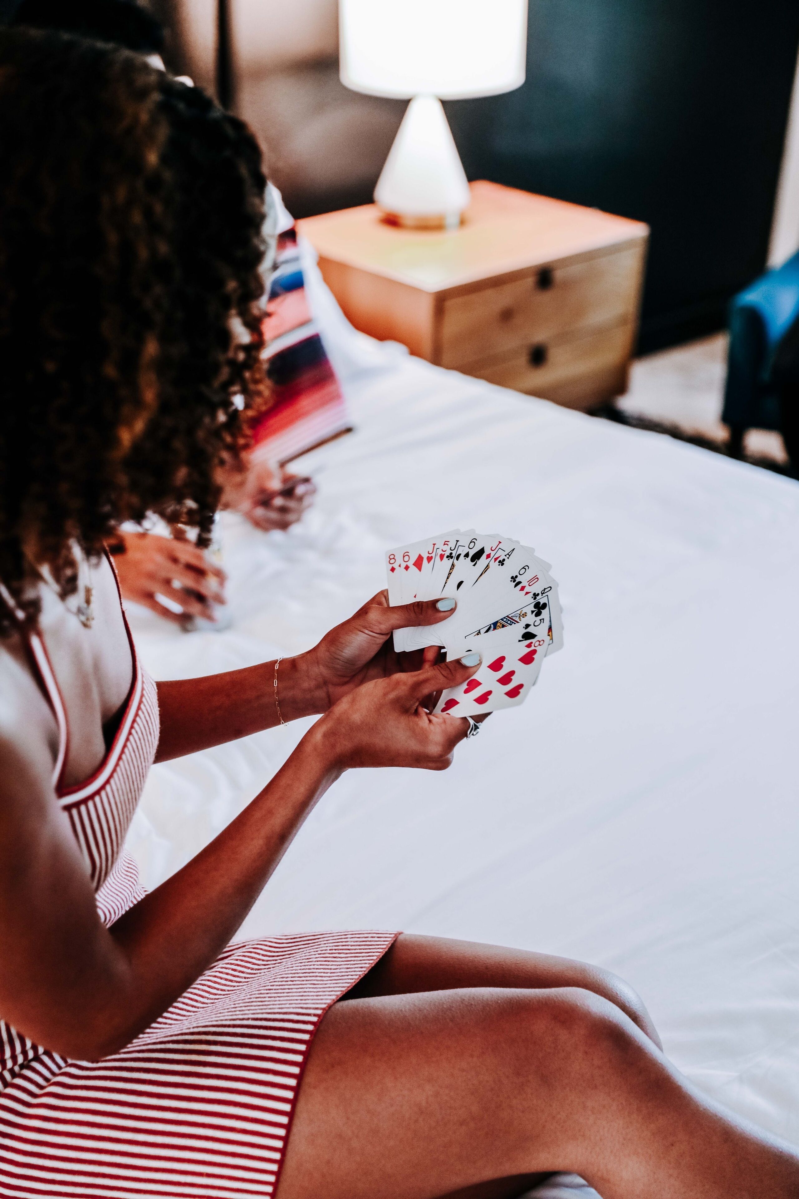 A person sitting on a bed holding playing cards.