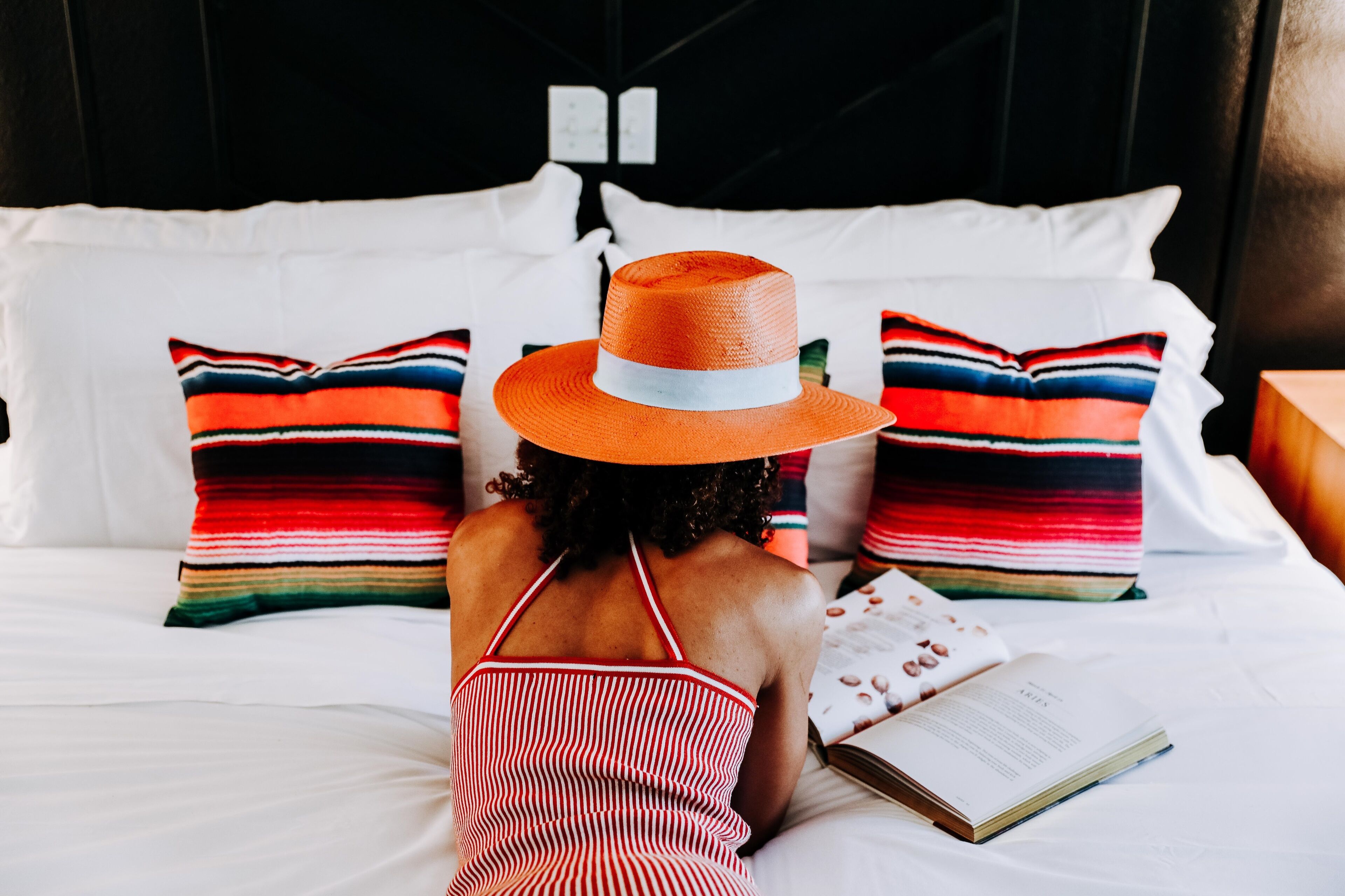 A person lying on a bed with striped pillows and a book, in a room with a black headboard and white bedding.