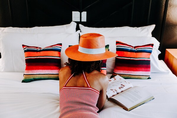 A person lying on a bed with striped pillows and a book, in a room with a black headboard and white bedding.