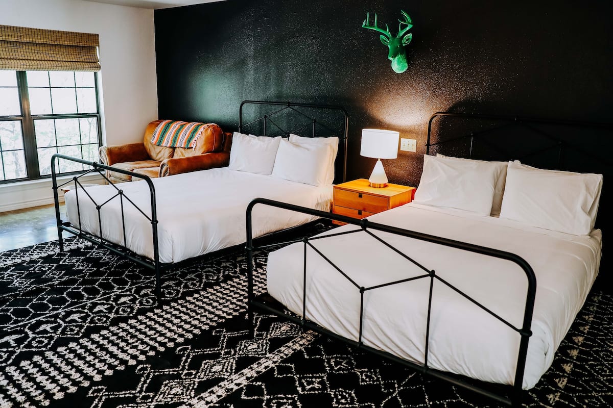 Quarto de hotel com duas camas, um tapete estampado, uma decoração de cabeça de veado fixada na parede e uma janela com vista.