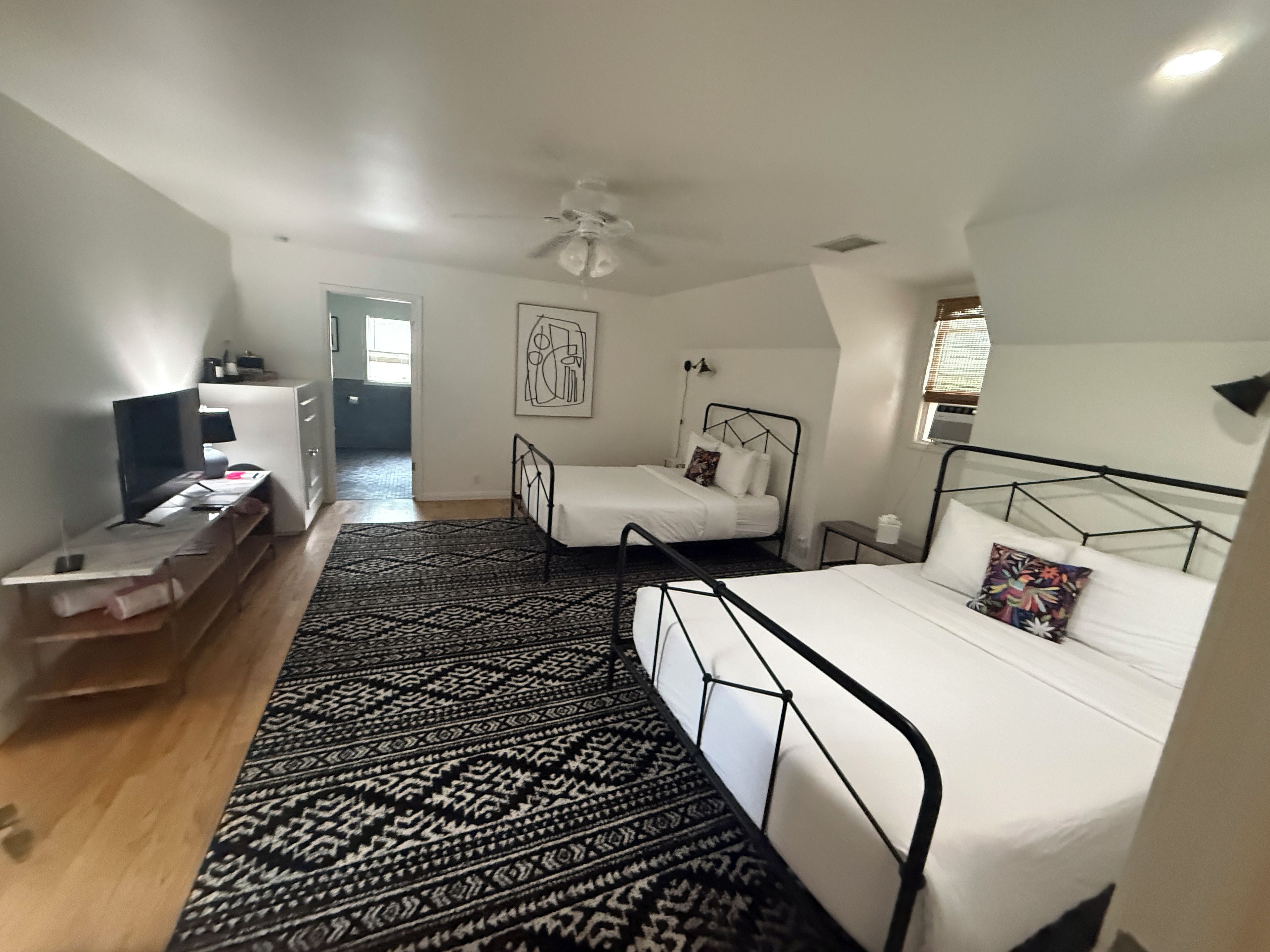 A bedroom with two beds, a desk, a chair, a ceiling fan, and a patterned rug.
