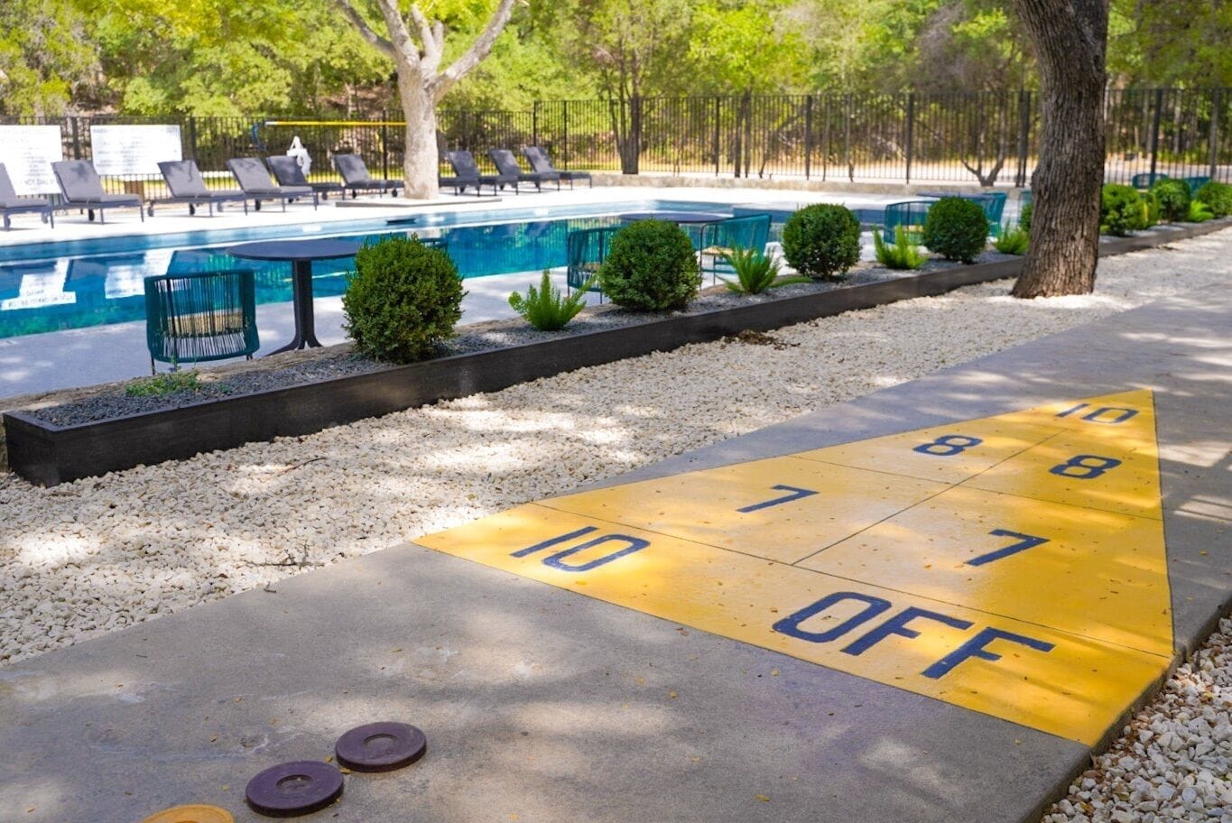 A pool area with a shuffleboard court and lounge chairs.