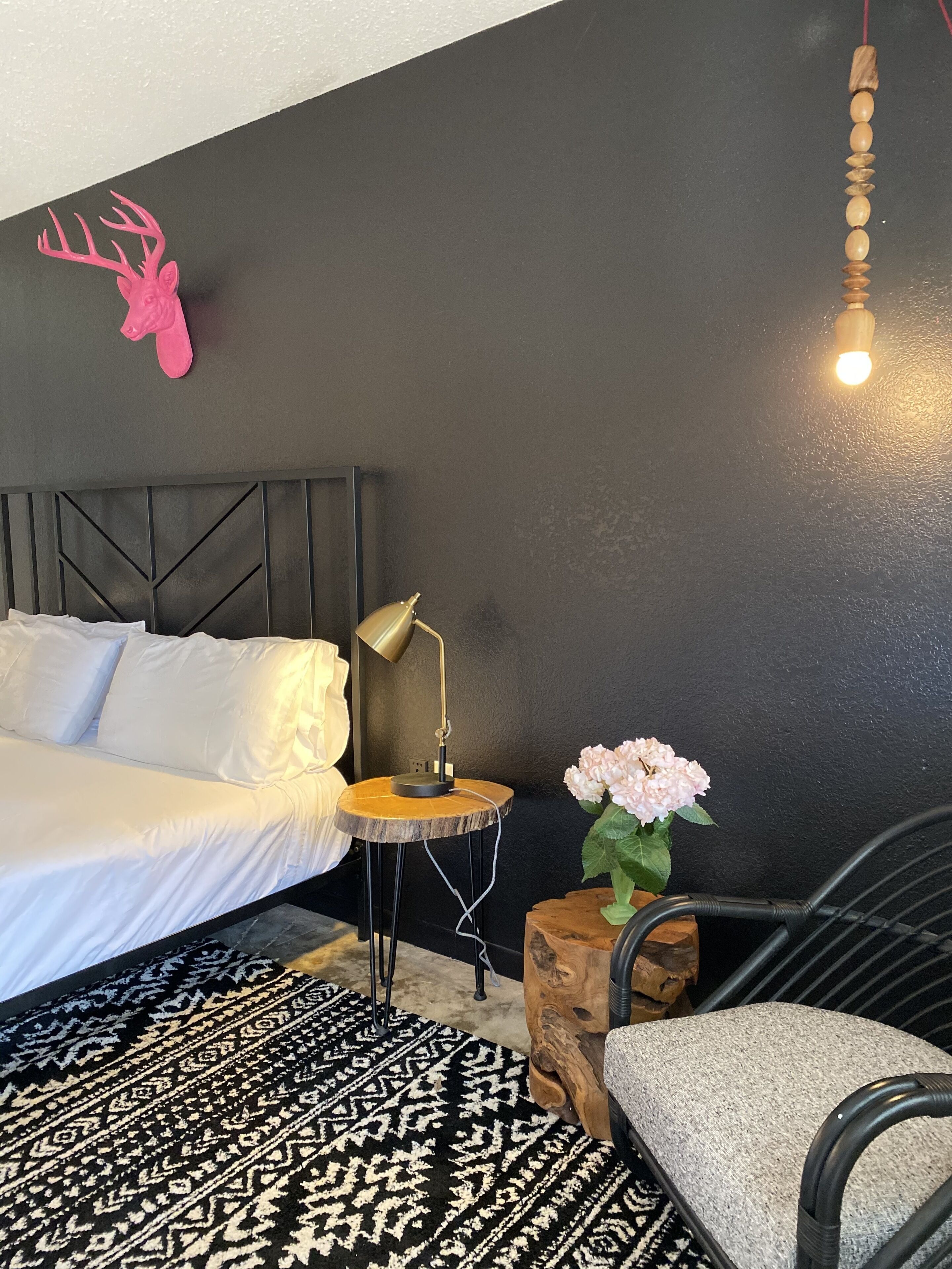 Une chambre moderne avec un lit, une lampe de chevet, une petite table ronde ornée d’un vase de fleurs, une tête de cerf décorative et une chaise.