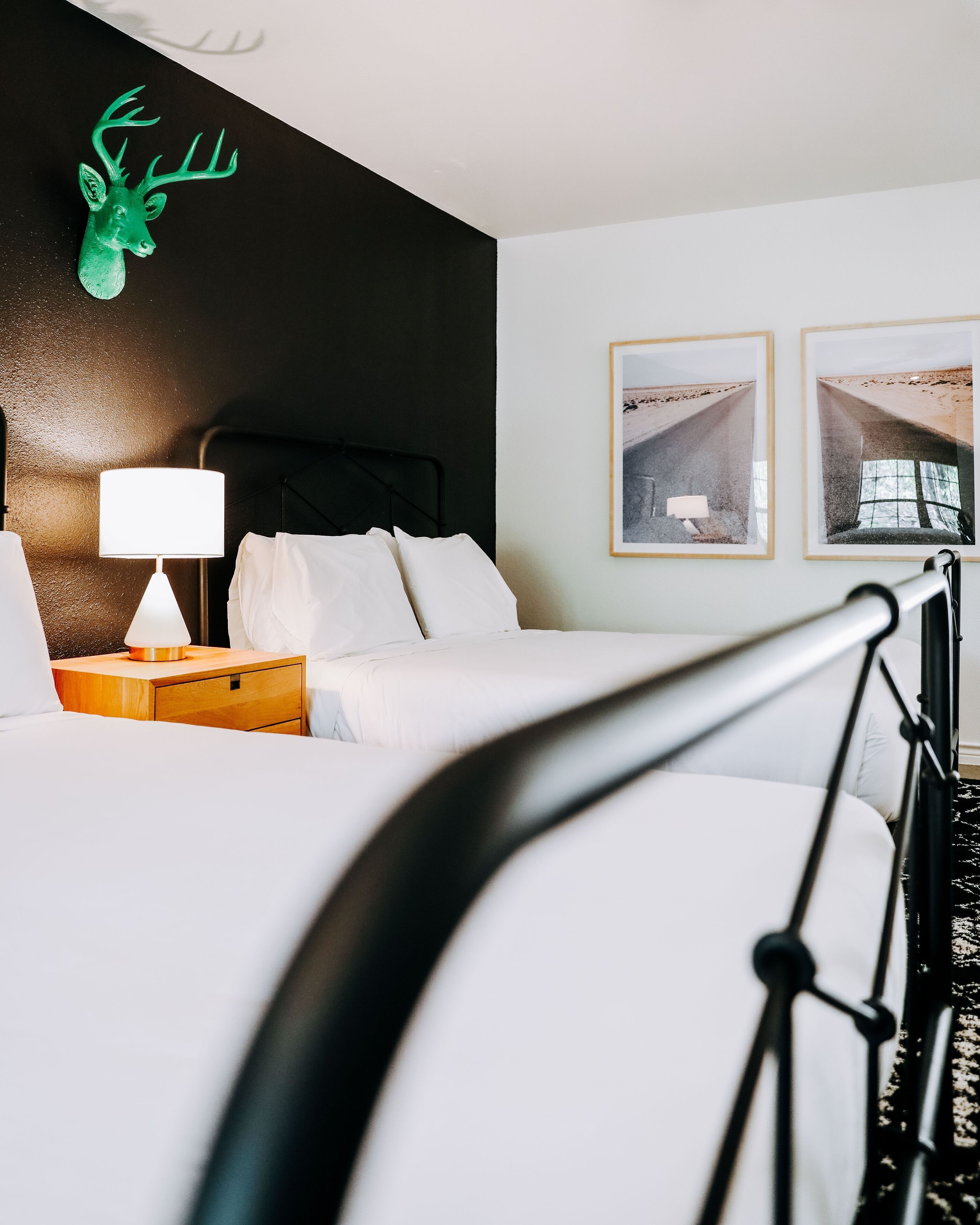 Een hotelkamer met een bed, een nachtkastje met lamp, een hoofdbord en twee ingelijste foto's aan de muur.