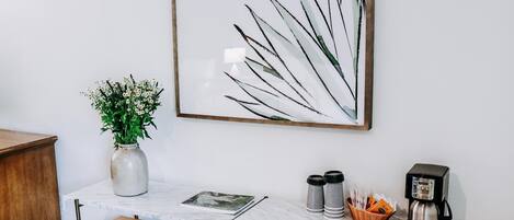 Una sala de estar moderna con una mesa de centro de mármol, un aparador de madera, un cuadro abstracto enmarcado, un jarrón con flores y una cafetera.