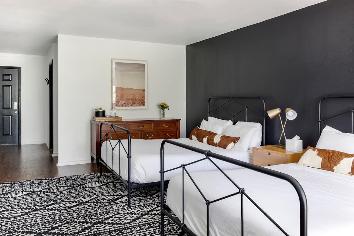 Quarto com duas camas, cômoda, mesa de cabeceira, abajur e quadro na parede.
