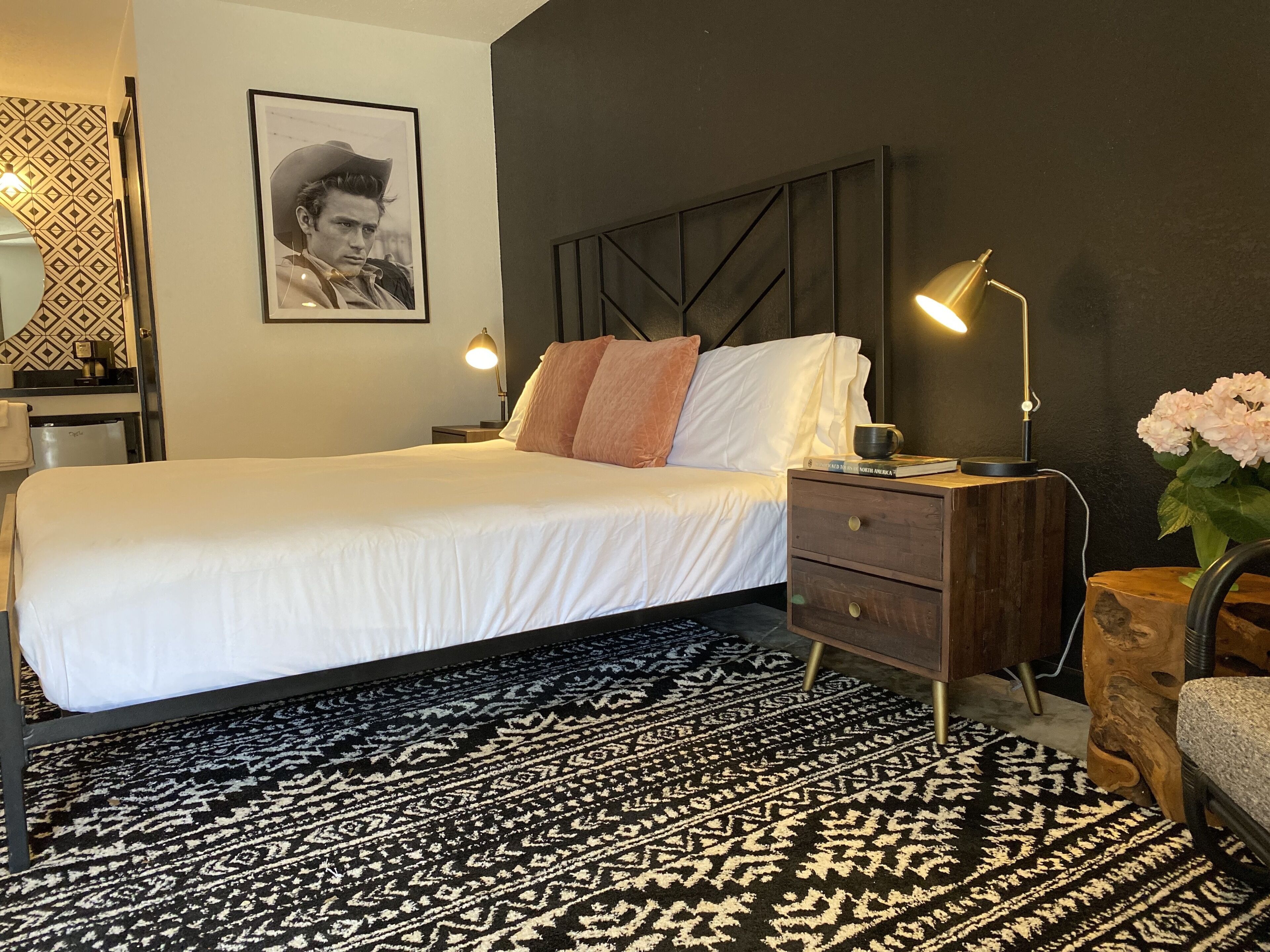 A neatly arranged bedroom with a bed, bedside lamps, a nightstand, a wooden side table, and a patterned rug.