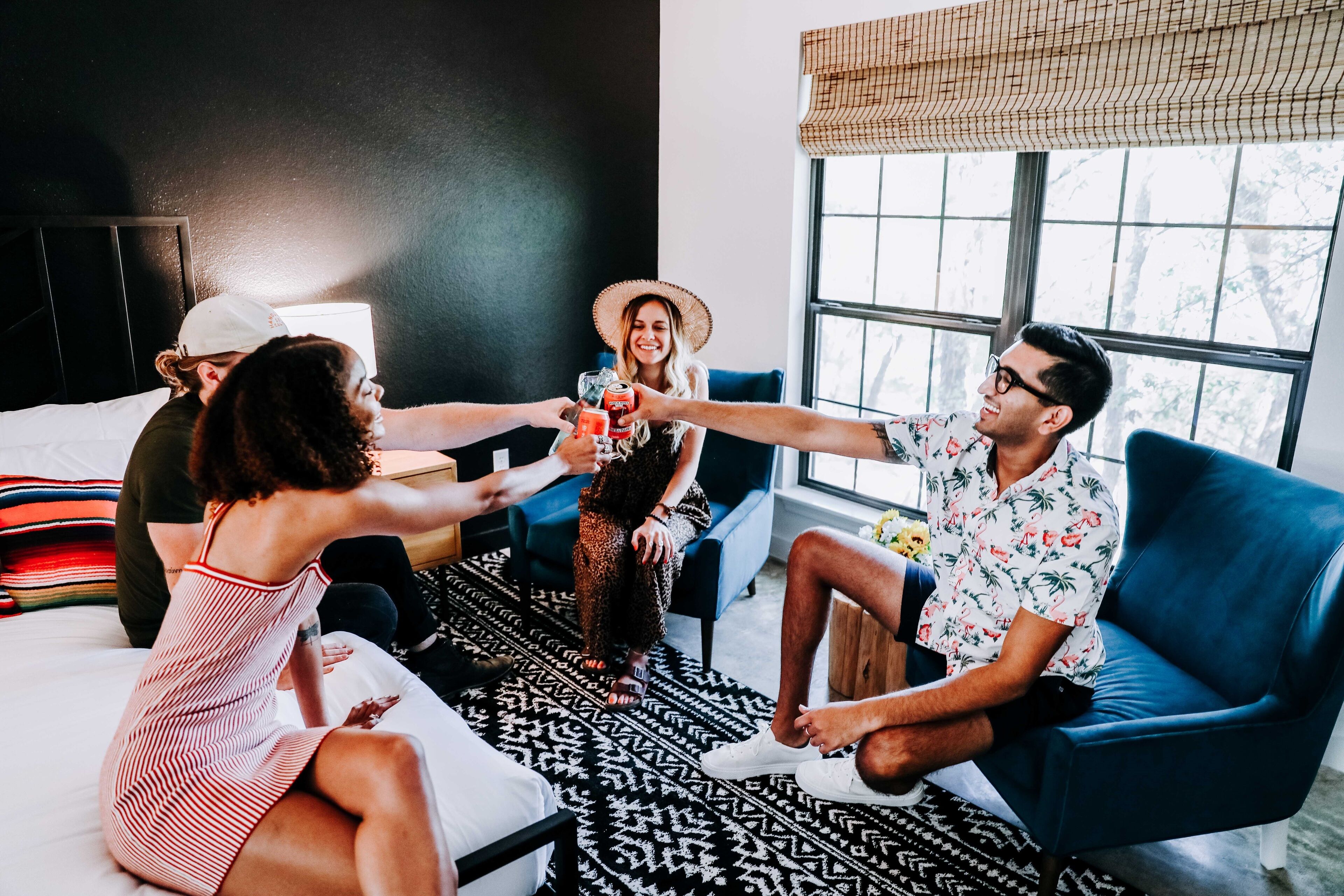 Un grupo de personas sentadas en una cama y un sofá en una habitación con un ventanal grande y una pared negra.