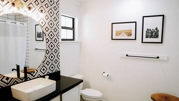 Un baño con pared de estampado blanco y negro, un lavamanos blanco, un inodoro y dos cuadros en la pared.