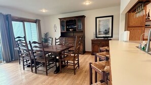Un comedor con una mesa y sillas de madera, un mueble con puertas de cristal y una encimera de cocina con un fregadero y utensilios.