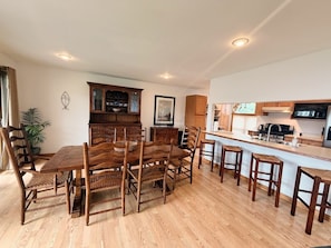 Una cocina moderna con armarios de madera, un comedor con una mesa grande y sillas, y una pequeña isla con taburetes.