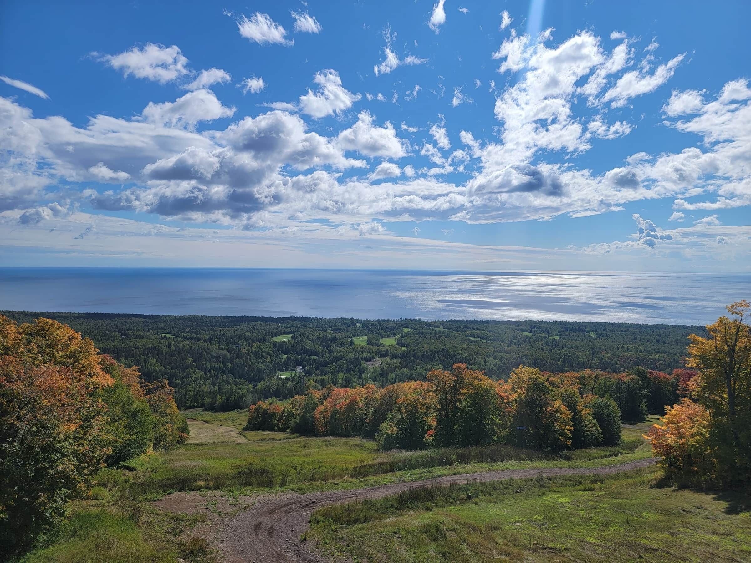 Vista panorâmica de uma paisagem costeira, com uma trilha de terra serpenteando por uma área arborizada.