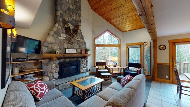 A cozy living room with a stone fireplace, comfortable seating, a television, and a large window offering a view of the outdoors. - Hibernation House at Lutsen, Hibernation House at Lutsen (Lutsen)
