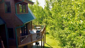 A wooden cabin with a balcony, outdoor seating, and a lush green forest backdrop. - Hibernation House at Lutsen, Hibernation House at Lutsen (Lutsen)