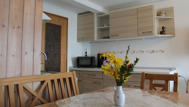 Een keuken met houten kastjes, een magnetron en een vaas met bloemen op tafel.