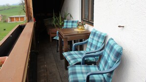 Een houten terras met een tafel, stoelen, een potplant en een uitzicht op een huis op de achtergrond.