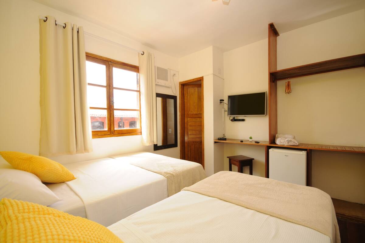 A hotel room with two beds, a TV, a small desk, and a refrigerator.
