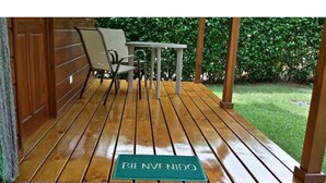 Um deck de madeira com um tapete de boas-vindas, uma mesa e cadeiras.