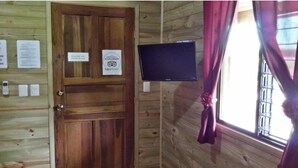 Quarto com painéis de madeira, porta de madeira, televisão montada e janela com cortinas.