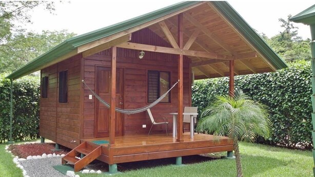 Uma cabana de madeira com varanda, rede e um pequeno espaço de estar ao ar livre.