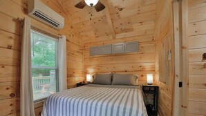 A wooden cabin room with a bed, bedside lamps, and an air conditioning unit. - Lena Cabin in Chattanooga's Premier Rustic Resort (Chattanooga)