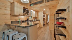 A wooden interior with a kitchen island, bar stools, a microwave, and a hanging rack. - Lena Cabin in Chattanooga's Premier Rustic Resort (Chattanooga)