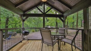 A covered outdoor deck with a table and chairs, a grill, and a view of the surrounding forest. - Lena Cabin in Chattanooga's Premier Rustic Resort (Chattanooga)
