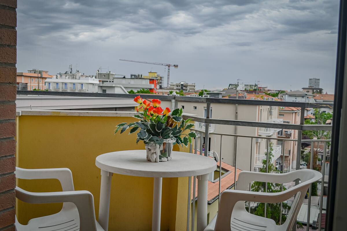 Varanda com uma mesa pequena, cadeiras, um vaso de planta e vista para a cidade.