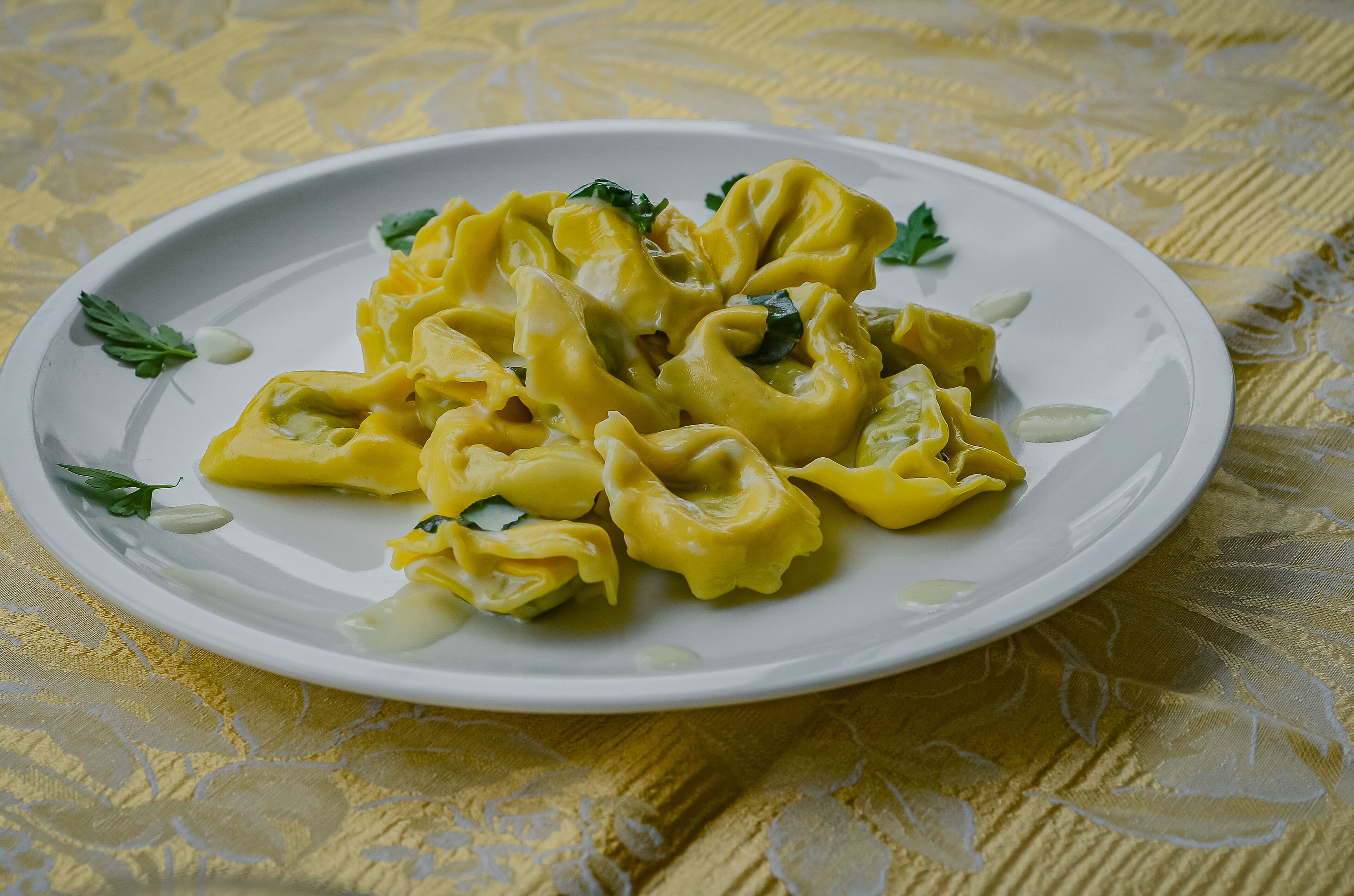 A plate of yellow dumplings with a garnish, placed on a table with a yellow patterned tablecloth.