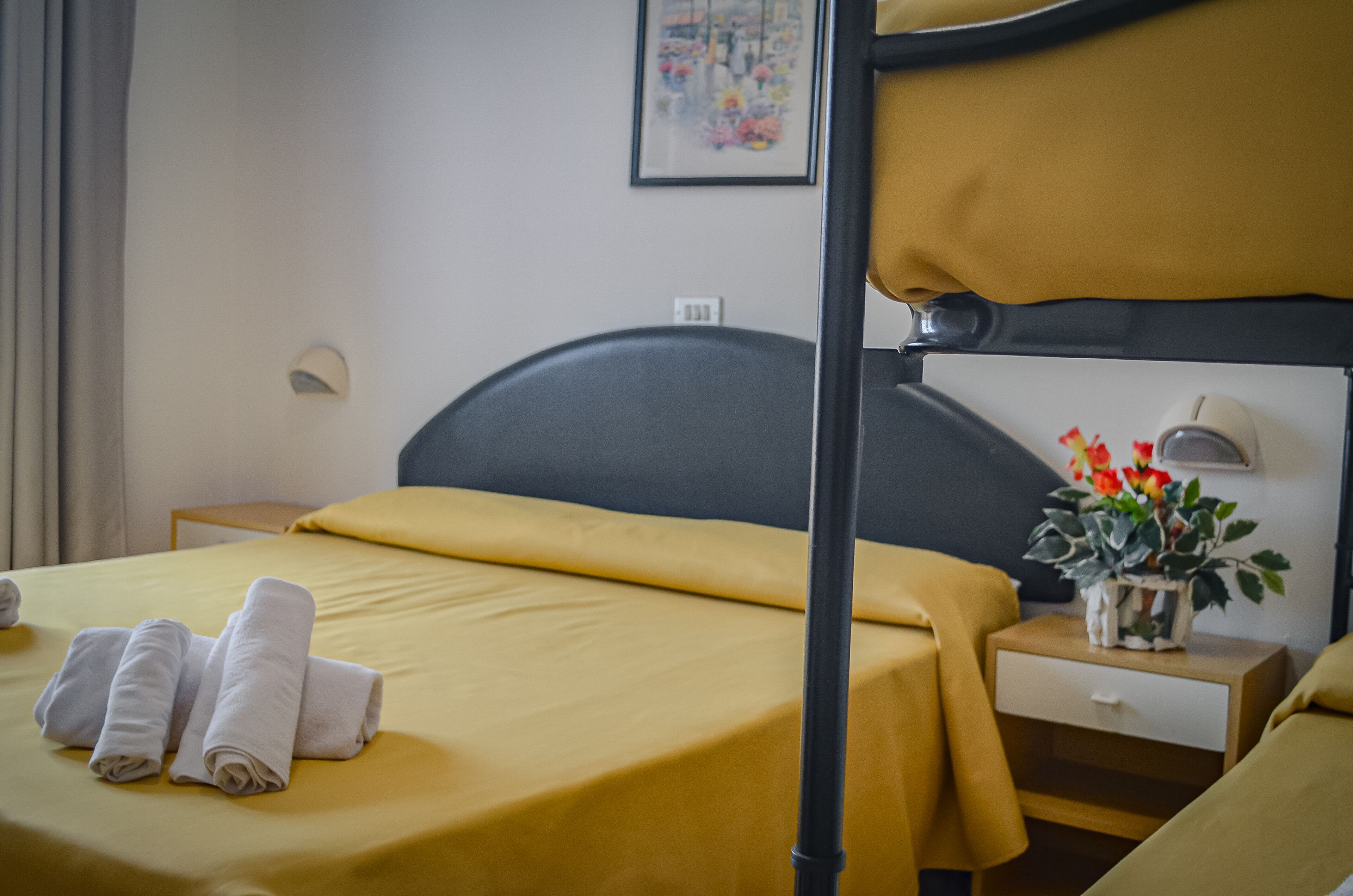 Habitación de hotel con literas, una mesita de noche con lámpara, un cajón pequeño y una planta en maceta.