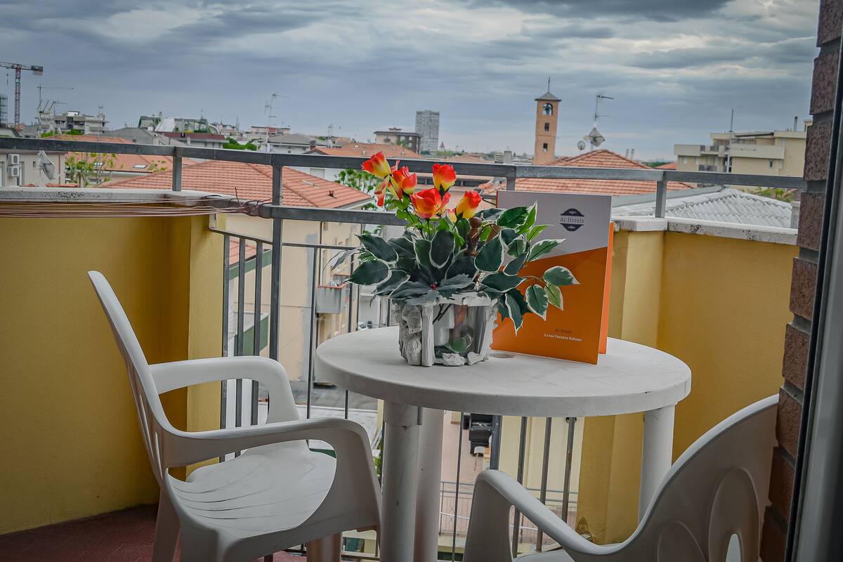 Uma varanda com mesa, cadeiras e um vaso com flores.