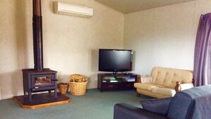 A living room with a fireplace, a television, a sofa, and a chair. - Irishman Drive Retreat, free wifi. (Twizel)