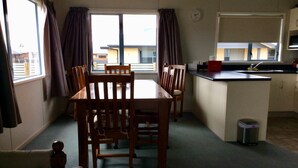 A dining area with a table and chairs, a small trash bin, and a kitchen area with a sink and cabinets. - Irishman Drive Retreat, free wifi. (Twizel)