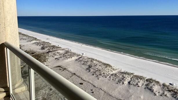 Blick auf einen Strand vom Balkon aus, mit blauem Himmel.