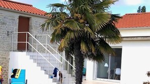 Ein Schwimmbecken mit glasklar blauem Wasser, eine Palme und ein Gebäude mit rotem Ziegeldach und einer Treppe, die zu einem Balkon führt.