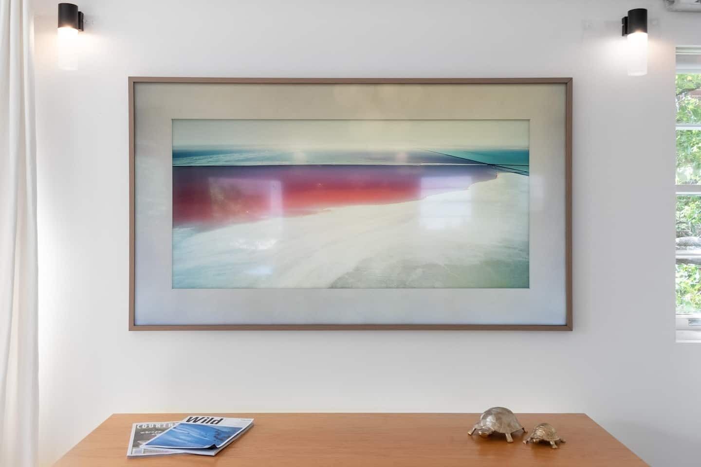 Un tableau abstrait encadré accroché au mur, une table en bois avec un magazine et une figurine de tortue, et deux appliques murales.