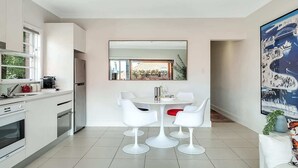 Eine moderne Küche mit weißen Schränken, ein Essbereich mit weißen Stühlen und ein großer Spiegel über dem Tisch.