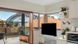 Ein modernes Wohnzimmer mit großem Fernseher, einem Glastisch und Blick auf die Sydney Harbour Bridge.
