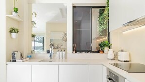 Une cuisine moderne avec des meubles blancs, un four encastré, une plaque de cuisson et une grande fenêtre offrant une belle vue.