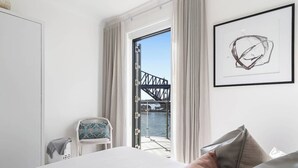 Une chambre d’hôtel avec un lit, une chaise, une vue sur un pont et une œuvre d’art encadrée au mur.