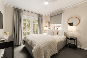 A hotel room with a large bed, two bedside tables, a desk, and a window with curtains.