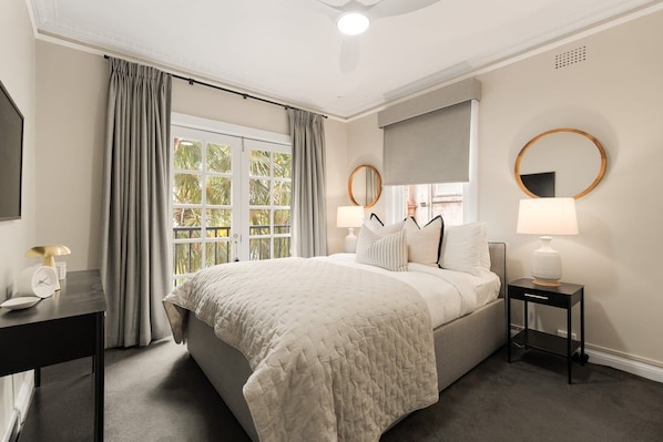 A hotel room with a large bed, two bedside tables, a desk, and a window with curtains.