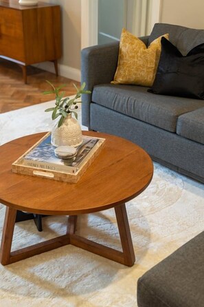 A round wooden coffee table with a book and a vase on top, placed on a white rug.