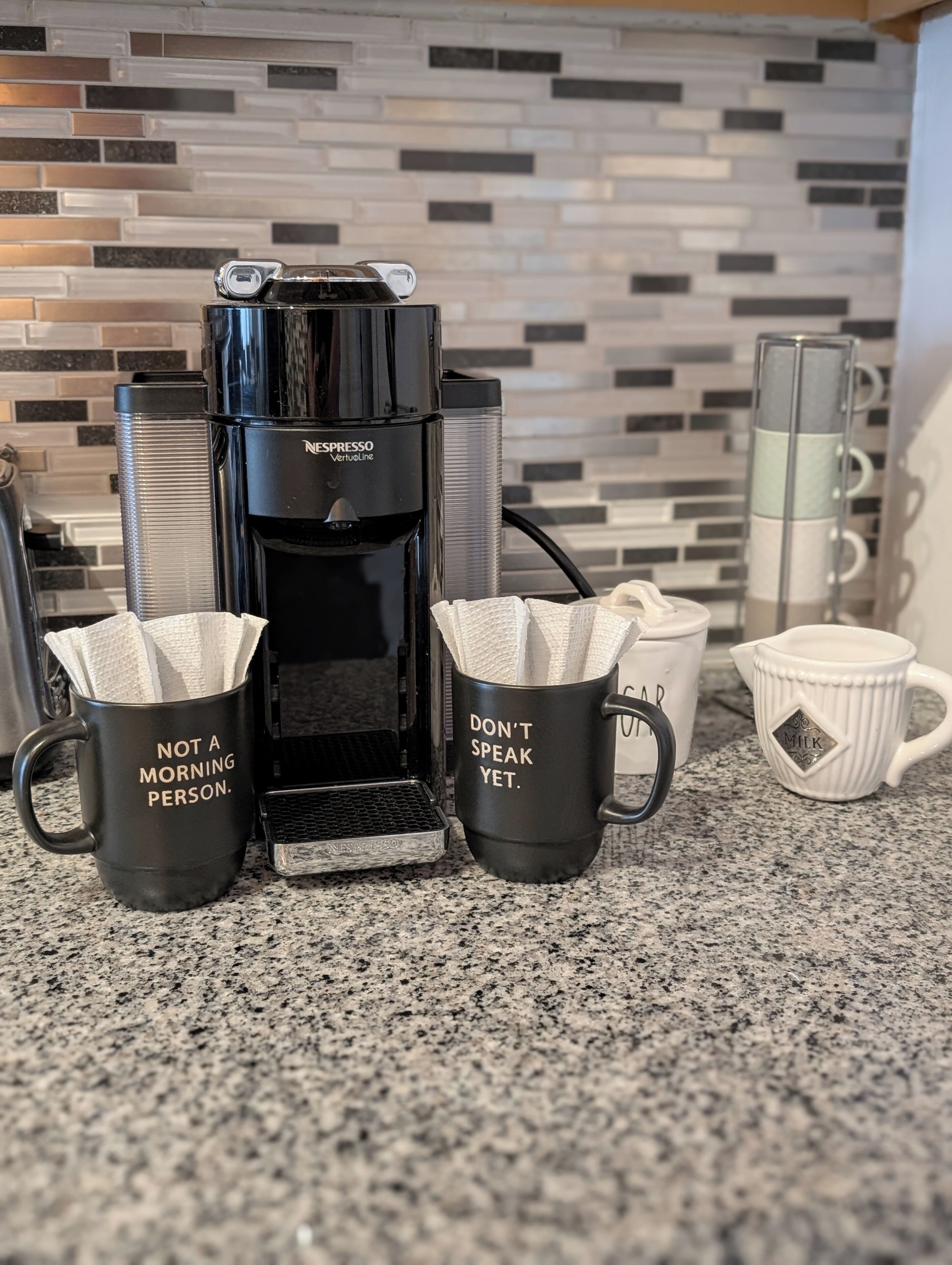 Une machine à café avec deux tasses devant, l’une portant une citation et l’autre un avertissement.
