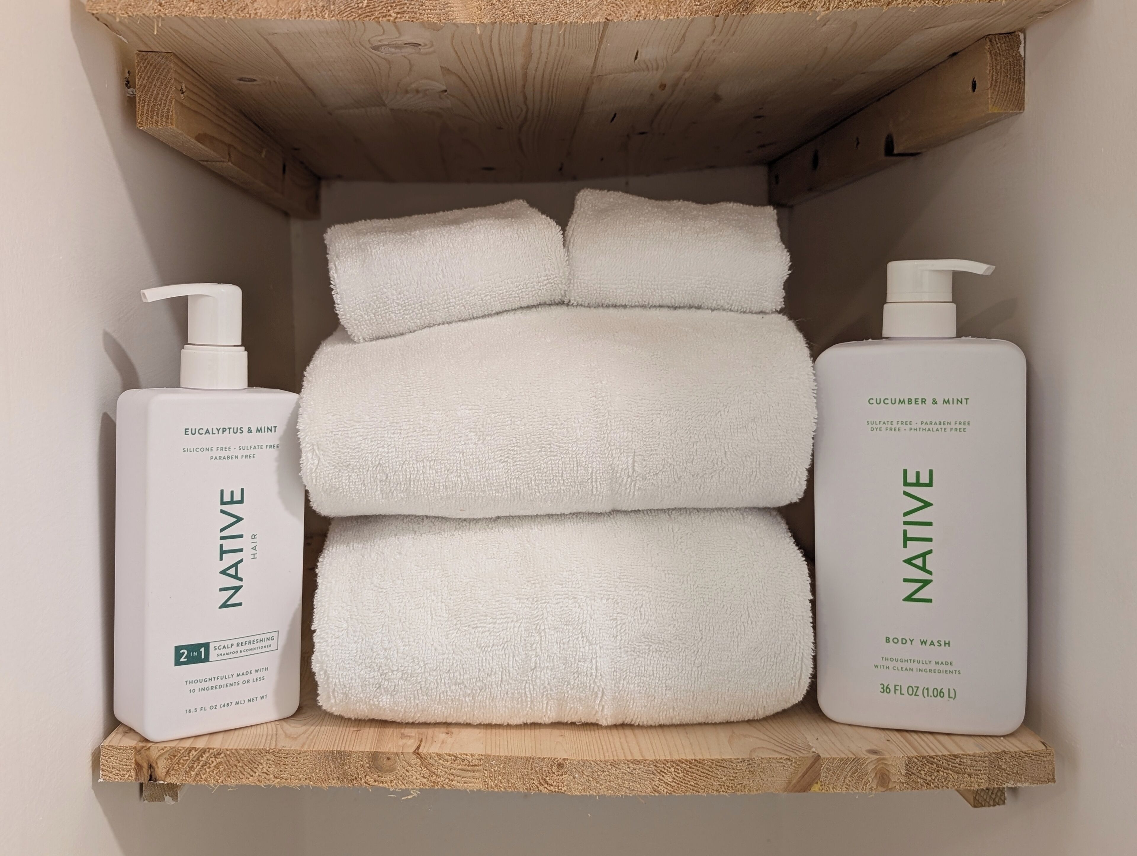 A shelf with two bottles of Native body wash and three folded towels.