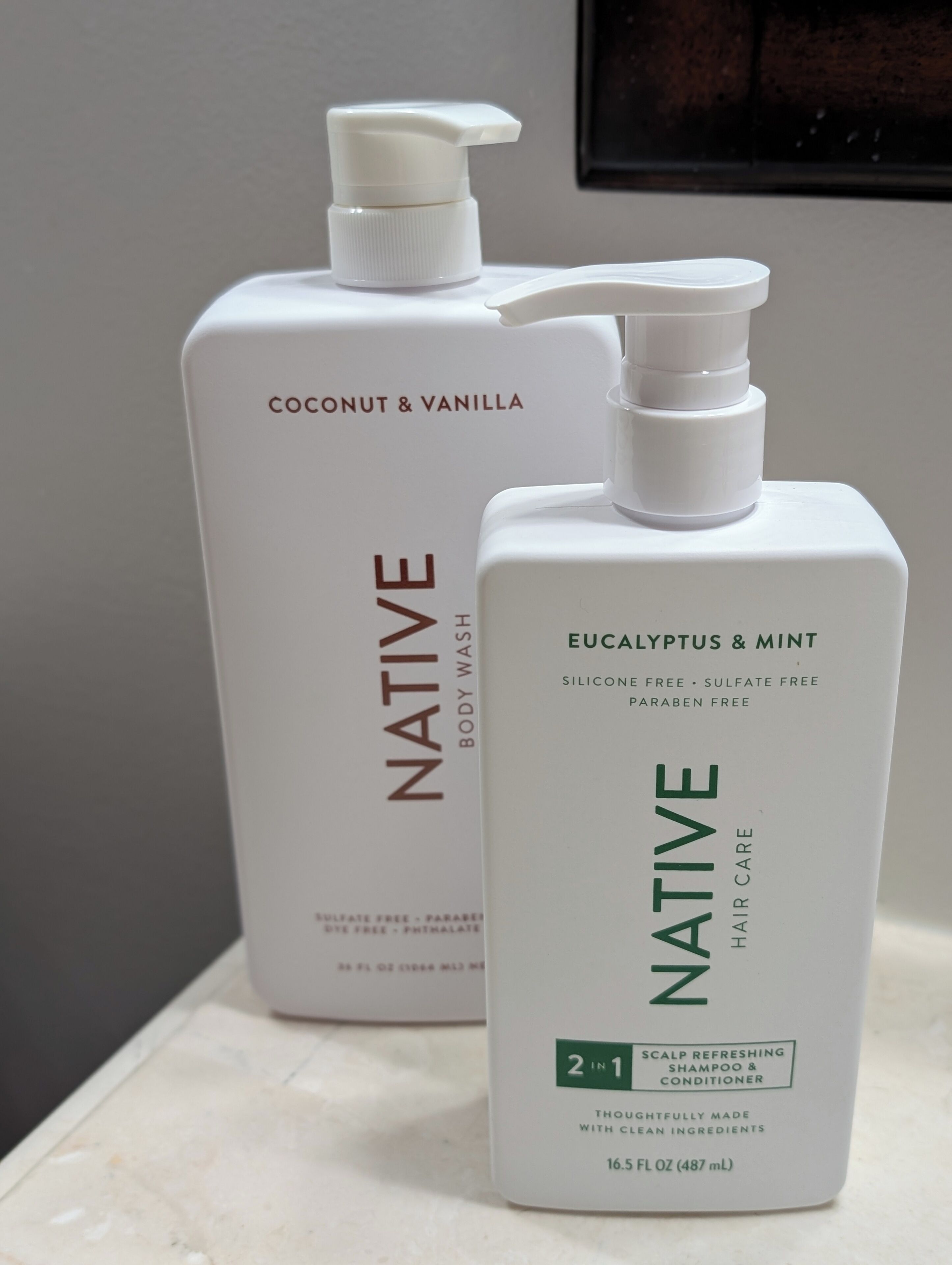Two bottles of Native body wash and conditioner on a bathroom counter.