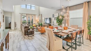A spacious living area with a dining table set for six, a sofa, and a TV. - 5BD/5BA Gorgeous Home w/ pool close to Disney (Kissimmee)