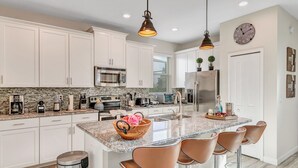 A modern kitchen with white cabinets, granite countertops, stainless steel appliances, and a central island with bar stools. - 5BD/5BA Gorgeous Home w/ pool close to Disney (Kissimmee)